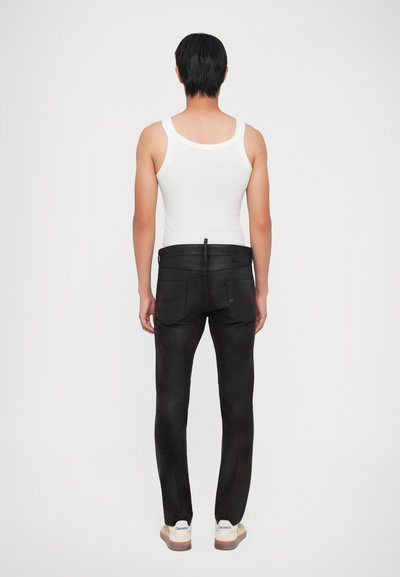 Jeans neri in denim con vestibilità slim, due tasche posteriori e una finitura testurizzata, abbinati a una canotta bianca e calzature casual.