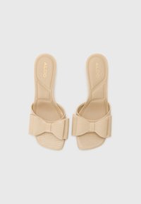 Beige slidesandaler med en teksturert stropp og en sløyfedetalj. Laget av syntetisk materiale. Flat såle uten hæl. Merkenavn preget.