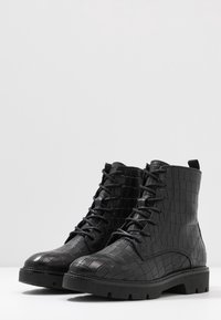 Bottines noires à lacets fabriquées en cuir effet crocodile texturé, avec une semelle robuste et des détails cousus.