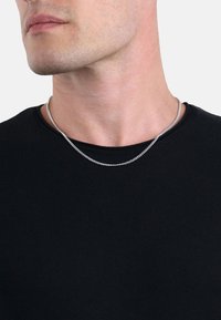 Collana in argento con una finitura liscia e lucida, indossata su una semplice maglietta nera a collo rotondo, che evidenzia il suo design elegante e la sua texture sottile.