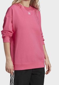 Rosa bomullströja med långa ärmar och rundad halsringning. Har vit Adidas-logga på bröstet, ribbade ärmslut och nederkant.