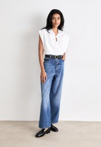 White sleeveless top with a keyhole detail, paired with high-waisted, light blue wide-leg denim jeans and black loafers.