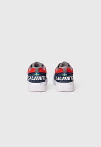 Chaussures de sport avec une tige en maille grise et textile rouge. Semelle blanche avec une texture antidérapante. Présente le logo et le drapeau suédois au niveau du talon.
