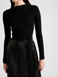 Fekete bordázott hosszú ujjú felső magas nyakkal, díszítő elemekkel díszítve, fekete flitteres, pliszírozott szoknyával és övvel párosítva.