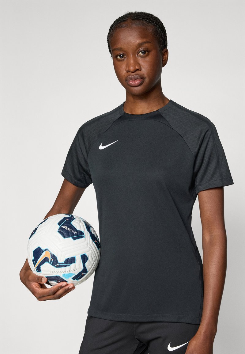 Maglietta atletica nera a maniche corte, con un design testurizzato sulle spalle e il logo Nike bianco. Tiene in mano un pallone da calcio con motivo.