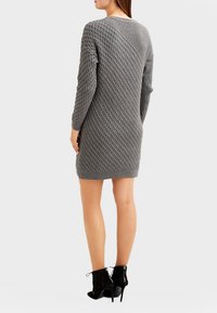 Graues gestricktes Kleid mit einem strukturierten Rautenmuster, langen Ärmeln und lockerer Passform, kombiniert mit schwarzen Schnür-Ankle-Boots.