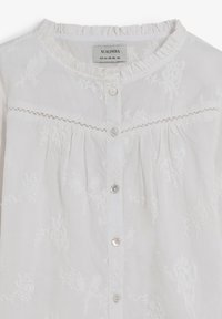 Blusa blanca con un cuello rizado, bordado floral y cierre de botones. Presenta detalles de botones y plisados. Textura suave.