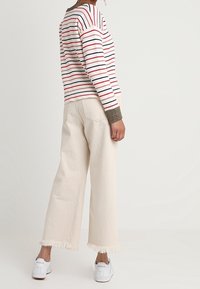 Pull rayé à manches longues en blanc, rouge et bleu ; associé à un pantalon large crème avec ourlets effilochés et des baskets blanches.