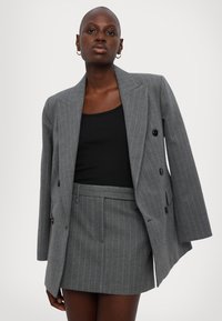 Blazer gris à rayures avec un large revers et un devant double boutonnage, associé à une jupe assortie à rayures. Tissu texturé, coupe structurée.