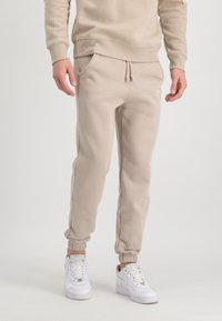 Beige sweatpants lavet af blødt stof, med elastisk talje og snor, sidelommer og elastiske ribkanter. Sammen med hvide sneakers.