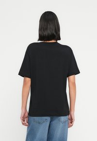 Μαύρο βαμβακερό T-shirt με άνετη εφαρμογή, κοντά μανίκια και κλασικό στρογγυλό λαιμόκοψη. Η πλάτη είναι απλή χωρίς ορατά λογότυπα.