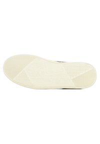 La semelle de la chaussure présente un design en caoutchouc blanc texturé avec des motifs variés, y compris des triangles et des motifs floraux, ainsi qu'une semelle intérieure rembourrée.