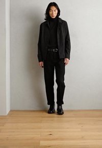 Black outfit featuring a textured button-up shirt, turtleneck, and straight-leg trousers, complemented by sleek black boots.