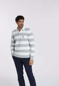 Pull-over en maille rayé gris et blanc à manches longues, avec un col, arborant un petit logo noir sur la poitrine gauche et des poignets côtelés.