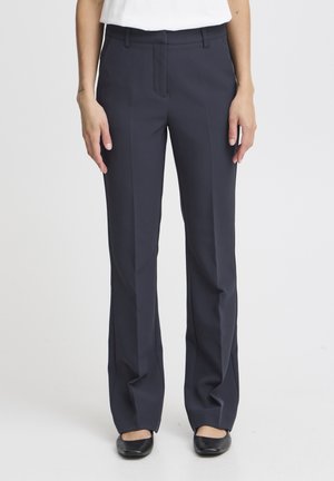 Pantaloni navy su misura con un design a gamba dritta, texture liscia e pieghe frontali, abbinati a scarpe nere basse.