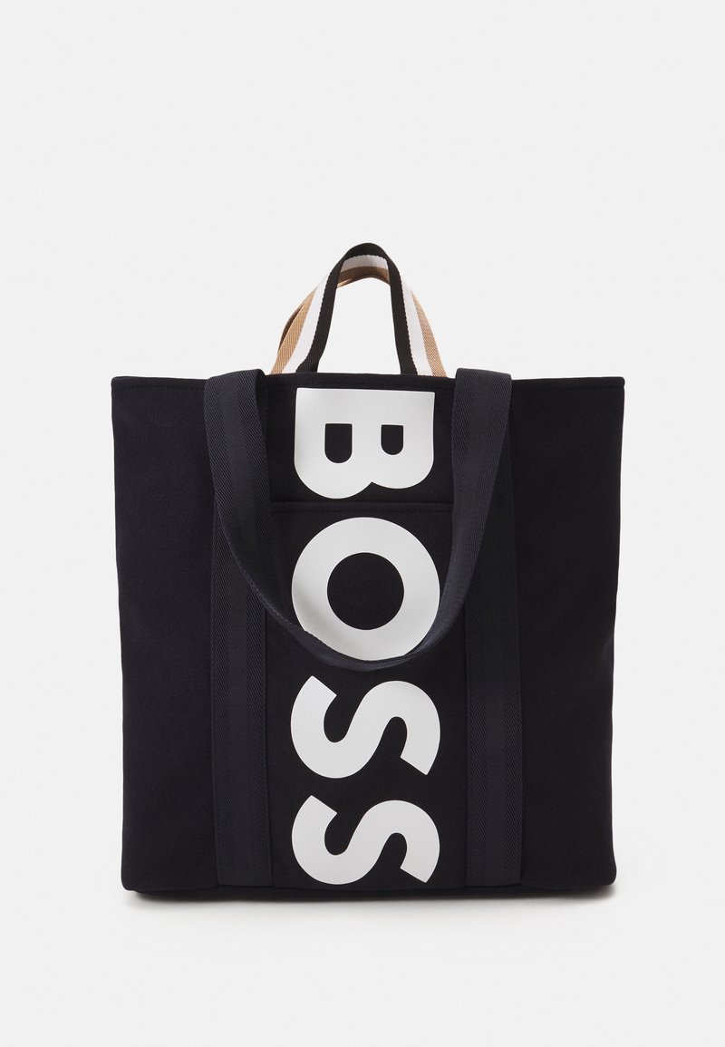 Sac cabas noir avec lettrage vertical blanc "BOSS" et double poignées, doté de bretelles de transport plus courtes en beige et noir sur le dessus.