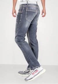 Graue Jeans aus Denim mit schlanker Passform, kontrastierenden Nähten und fünf Taschen. Getragen mit schwarz-weißen Sneakers im Muster.