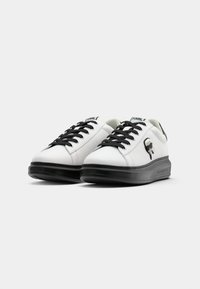 Białe skórzane sneakersy z czarnymi sznurowadłami i podeszwą. Posiadają czarny detal logo po boku oraz zaokrąglony kształt. Teksturowana gumowa podeszwa.