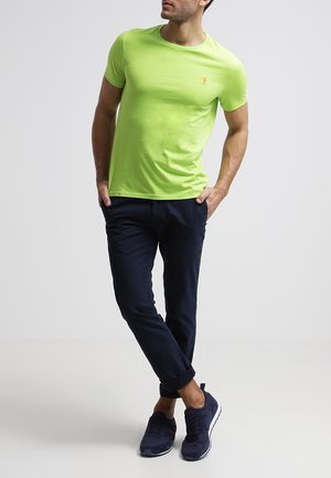 Tajemně zelené tričko s krátkým rukávem a kulatým výstřihem, v kombinaci s námořnickými chinos kalhotami a tmavými teniskami, které ukazují pohodlný střih.