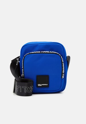 Kompakt blå crossbody taske med sort justerbar rem og frontlomme, mærket med hvide Karl Lagerfeld Jeans-logoer.