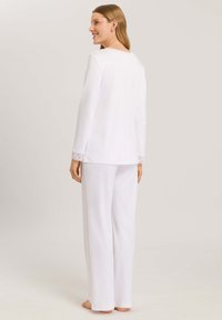 Bílý set domácího oblečení, který obsahuje top s dlouhými rukávy a krajkovými detaily na manžetách, spolu se širokými kalhotami, vyrobený z měkké látky.