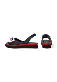 Slingback sandalen met een bovenwerk van zwart leer, rode zool, witte en rode accenten, en decoratieve hardware aan de voorkant. Plat, lichtgewicht ontwerp.