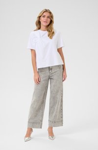 T-shirt blanc à manches courtes avec un design avant torsadé, associé à un jean gris taille haute à jambes larges et des escarpins argentés à bout pointu.