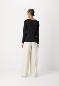 Svart langermet topp med rund hals, kombinert med lyse beige vide bukser. Glatt stoff, minimal detaljer, tettsittende silhuett.
