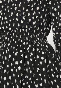 Černé šaty s bílým tečkovaným vzorem, s nařaseným pasem a strukturovanou tkaninou. Dlouhé rukávy obohacují design.