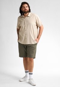 Korte mouwen beige overhemd met knopen, olijfgroene shorts, witte sneakers met zwart gestreepte sokken. Casual pasvorm met een ontspannen ontwerp.