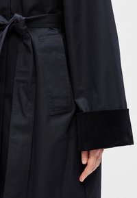 Ναυτικό παλτό με ζ�ώνη για δέσιμο, λείο ύφασμα και μανσέτα από κορδόνι. Διαθέτει τσέπη με πατς και διακριτική λεπτομέρεια λογότυπου.