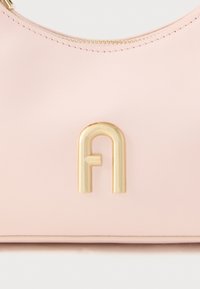 Rozā ādas soma ar gludu tekstūru un apaļu formu, kurai ir zelta metāla logotipa akcenti un rāvējslēdzēja aizdare augšpusē.