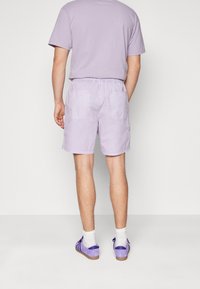 Levandulové bavlněné kraťasy s elastickým pasem, dvěma zadními kapsami, nošeny s bílými ponožkami a fialovými botami, doplněné o odpovídající vršek.