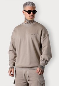 Sweatshirt beige en tissu doux avec un col rond et des poignets côtelés. Présente un petit logo "ESTEEM" sur la poitrine et une coupe décontractée.