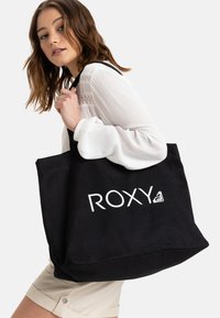 Černá plátěná taška s bílým logo "ROXY", prostorný design, pevné uši a měkká textura. Vhodná pro každodenní nošení.