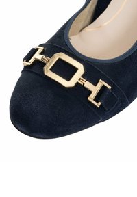 Marineblauwe suède instappers met een ronde neus, voorzien van een gouden geometrische gesp en een banddetail over de voorkant voor accentuering.