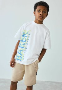 Hvid bomulds t-shirt med multicolor grafisk tekst "BAKER BY TED BAKER" på fronten; parret med beige shorts med sidelommer.