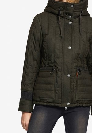 Dark green quilted jacket with front snap buttons, zippered pockets, drawstring hood, and ribbed cuffs worn with dark jeans.