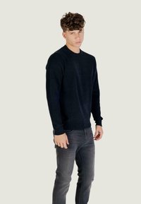 Mornarska dukserica s okruglim izrezom napravljena od mekog pletiva, s dugim rukavima i rebrastim rubovima, u kombinaciji s tamnosivim trapericama.