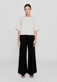 Lichtroze top met korte mouwen, gecombineerd met hoge zwarte wijde broek. De outfit heeft een losse fit en een minimalistisch ontwerp.