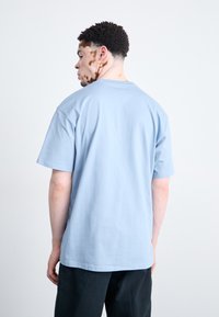 Light blue cotton T-shirt with a relaxed fit, short sleeves, and a crew neckline, displayed from the back on a neutral background.