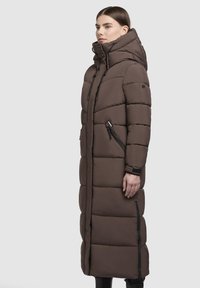 Garšs brūns polsterēts mēteli ar augstu apkakli, vertikālu šuvumu un melna zippu akcentiem. Iespējas noņemt kapuci un sānu kabatas.