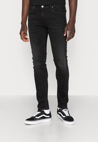 Černé skinny džíny s jemnými odrbanými místy, spárované s černobílými teniskami s klasickým designem a bílými akcenty.
