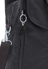 Schwarzer Stoff-Rucksack mit Reißverschluss, silbernen Beschlägen und einem kleinen schwarzen Schlüsselanhänger. Strukturierte Oberfläche und verstellbarer Tragegurt.