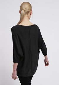 Schwarz, übergroßer Pullover mit einem Bootsausschnitt, Dreiviertelärmeln und einer Mittelnaht auf der Rückseite; weiche Textur.