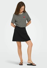 Zwarte A-lijn rok gecombineerd met een zwart-wit gestreept T-shirt met een rood hartlogo. De stof lijkt zacht en casual.
