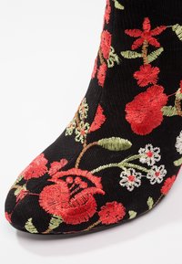 Schwarze Stoff-Ankle Boots mit lebhafter roter und weißer Blumenstickerei, einzigartiger Textur, spitzer Zehenform und schnittiger Passform.
