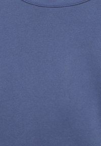 Gros plan sur un tissu bleu uni avec une texture tricotée visible et une couture arrondie près du bord supérieur.