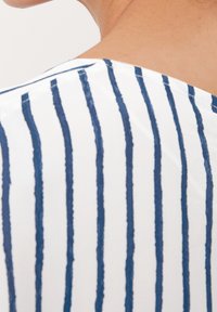 Tessuto bianco con strisce verticali blu navy, con scollatura a barchetta e superficie liscia, che presenta una leggera lucentezza.