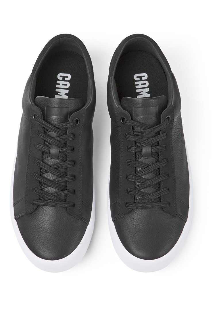 Zapatillas de cuero negras con una textura suave, que presentan un diseño de cordones y suelas de goma blancas en contraste. Logo de la marca visible en el interior.